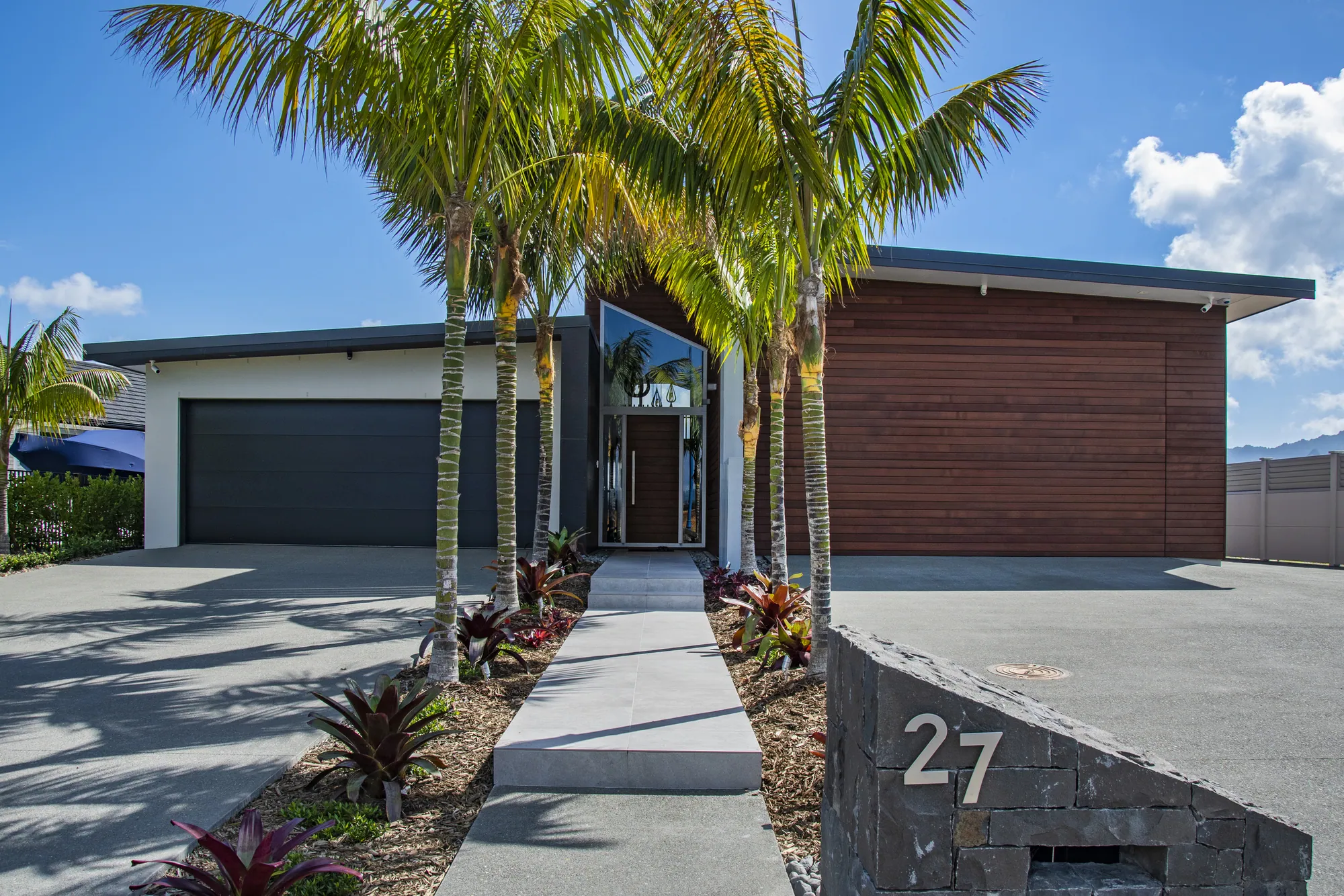 Entry path between palms to a home with a cedar-clad garage wing