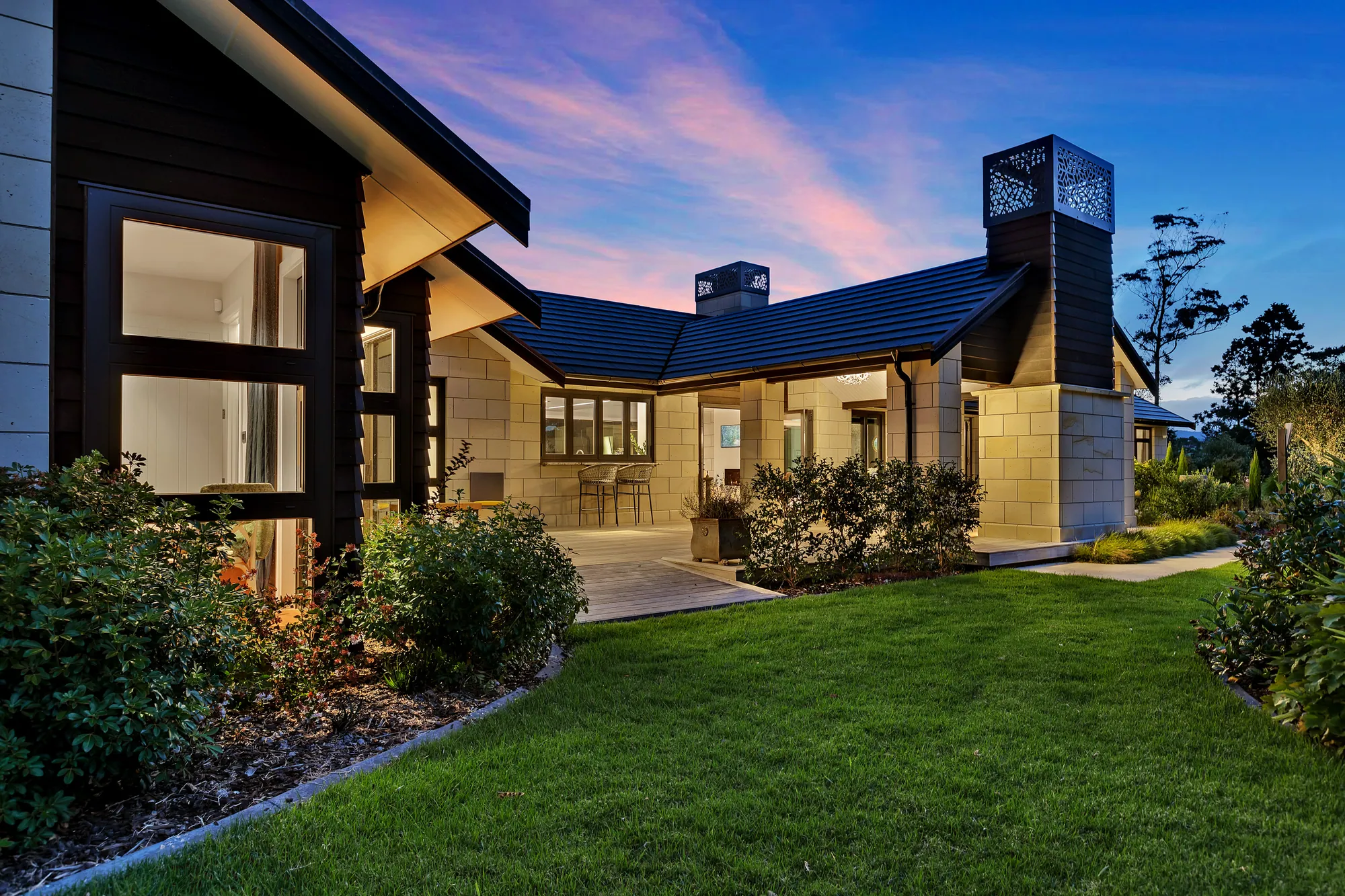 Stone-clad home with dark window frames and lawn at dusk