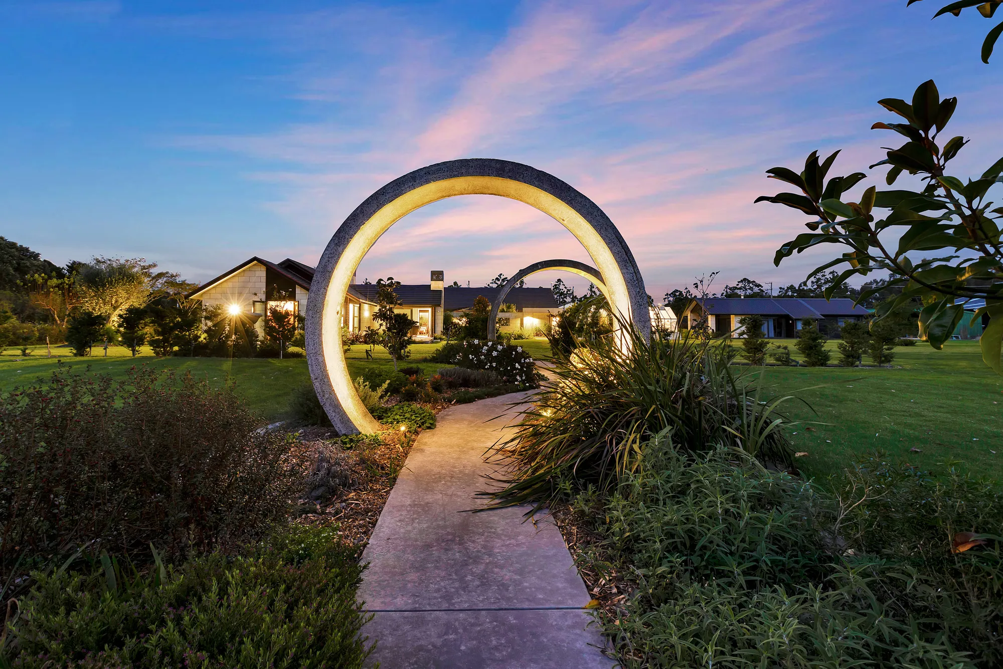 Circular garden arch lit at dusk on the path to the house