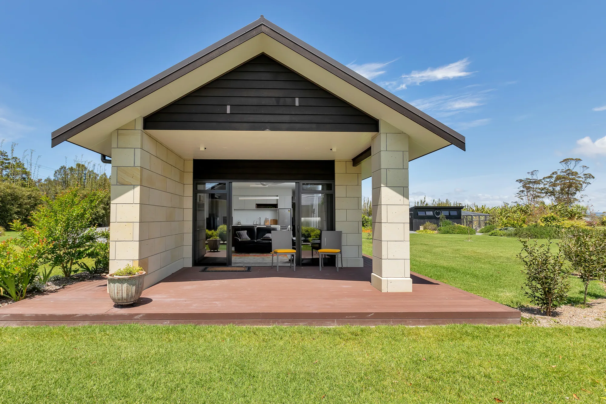Gabled outdoor room with stone columns opening to the lawn