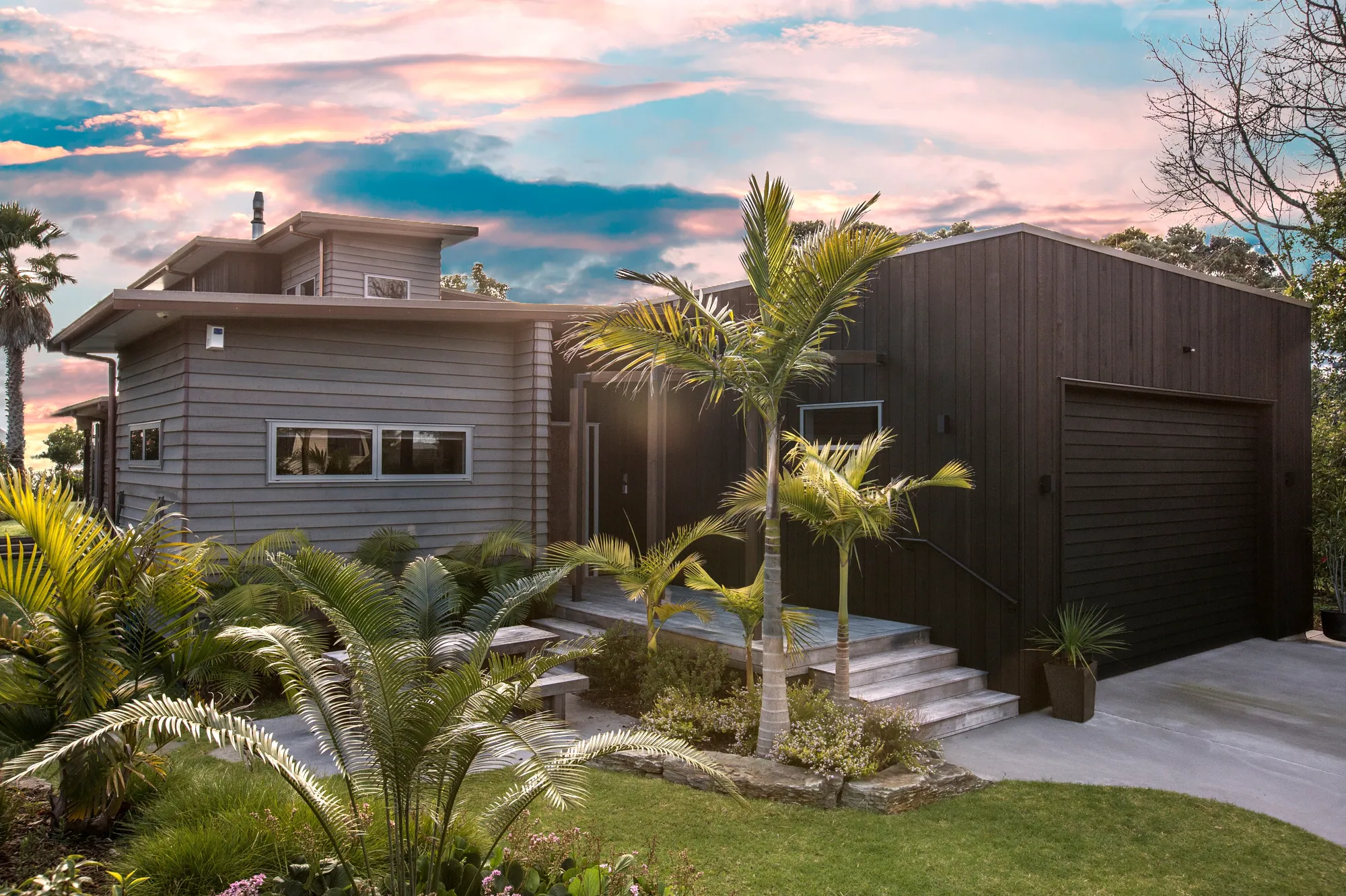 Dark-clad home with palms and planted steps at sunset