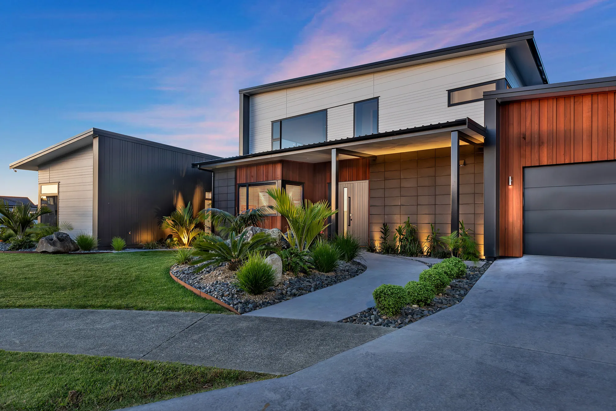 Two-storey home with cedar and dark cladding lit at dusk