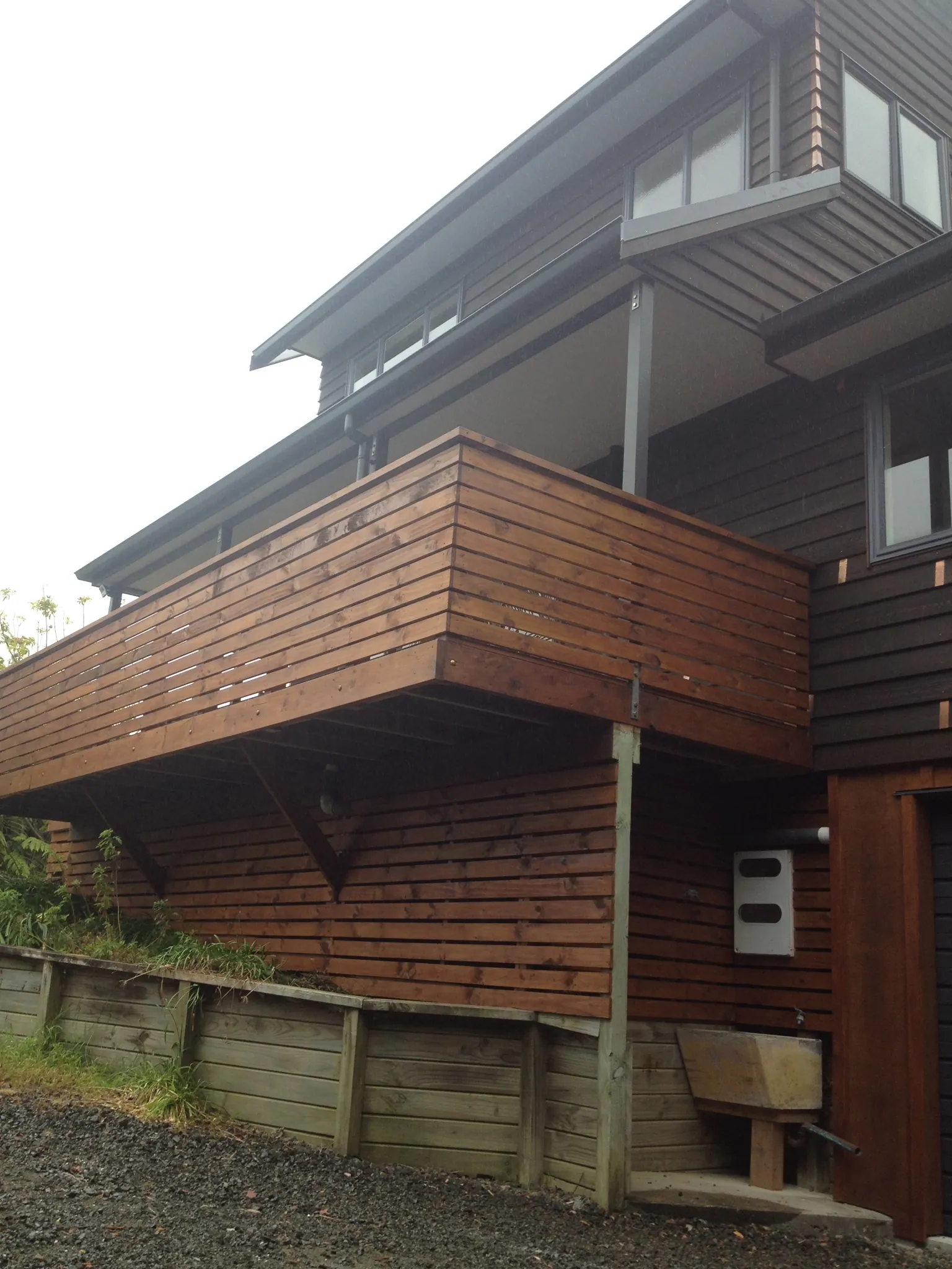 Stained timber cladding and deck on a hillside reclad