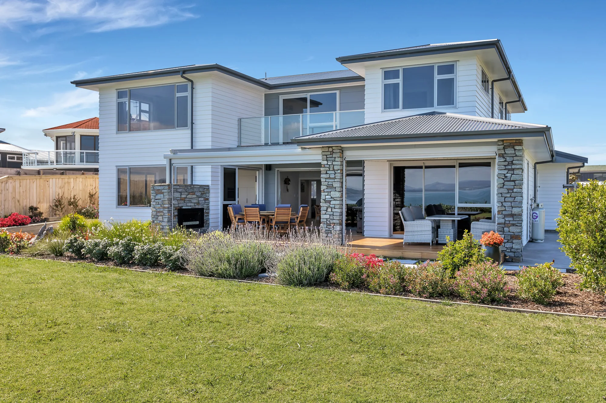 Two-storey weatherboard home with schist columns, seen across the garden