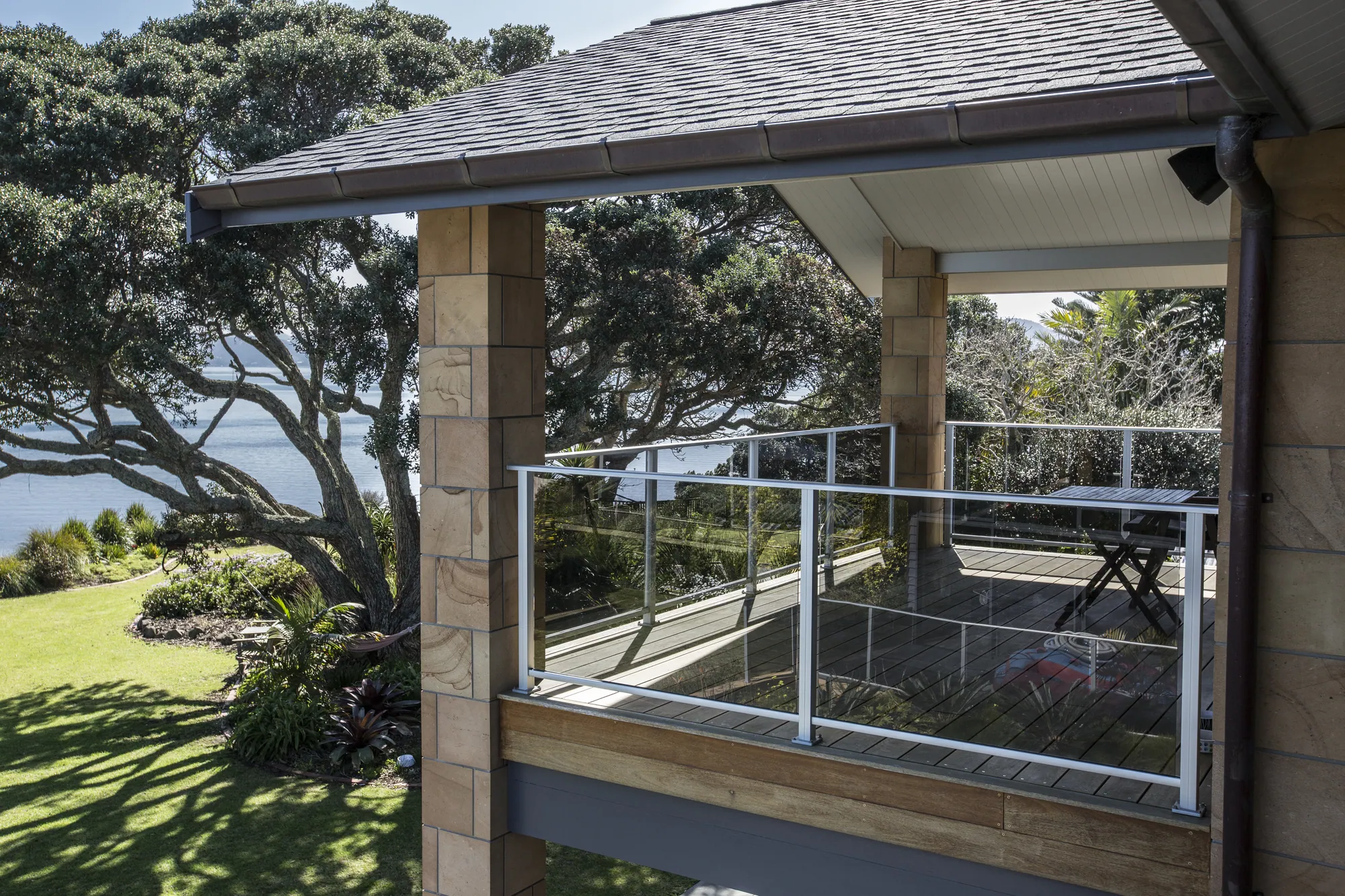 Covered balcony with glass balustrade among pohutukawa above the water