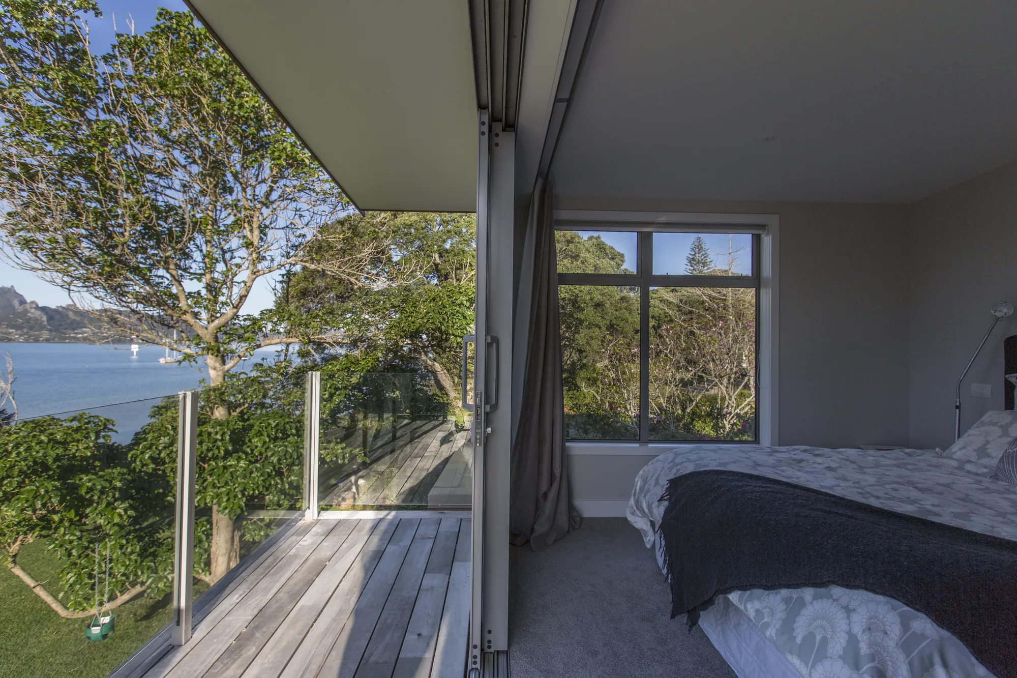 Bedroom opening to a balcony and the harbour through the trees