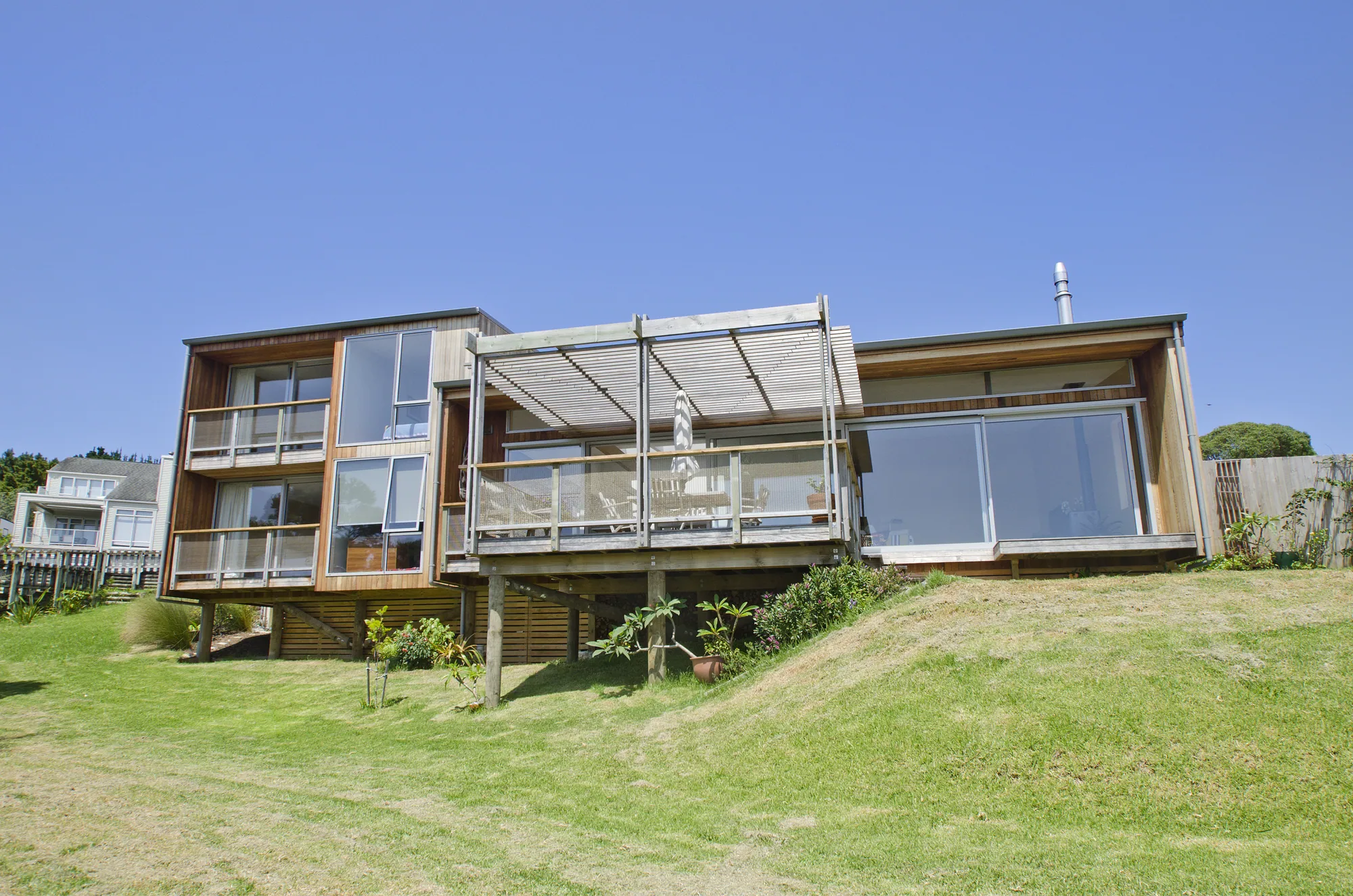 Cedar and dark-clad home with a deck and pergola above a sloping lawn