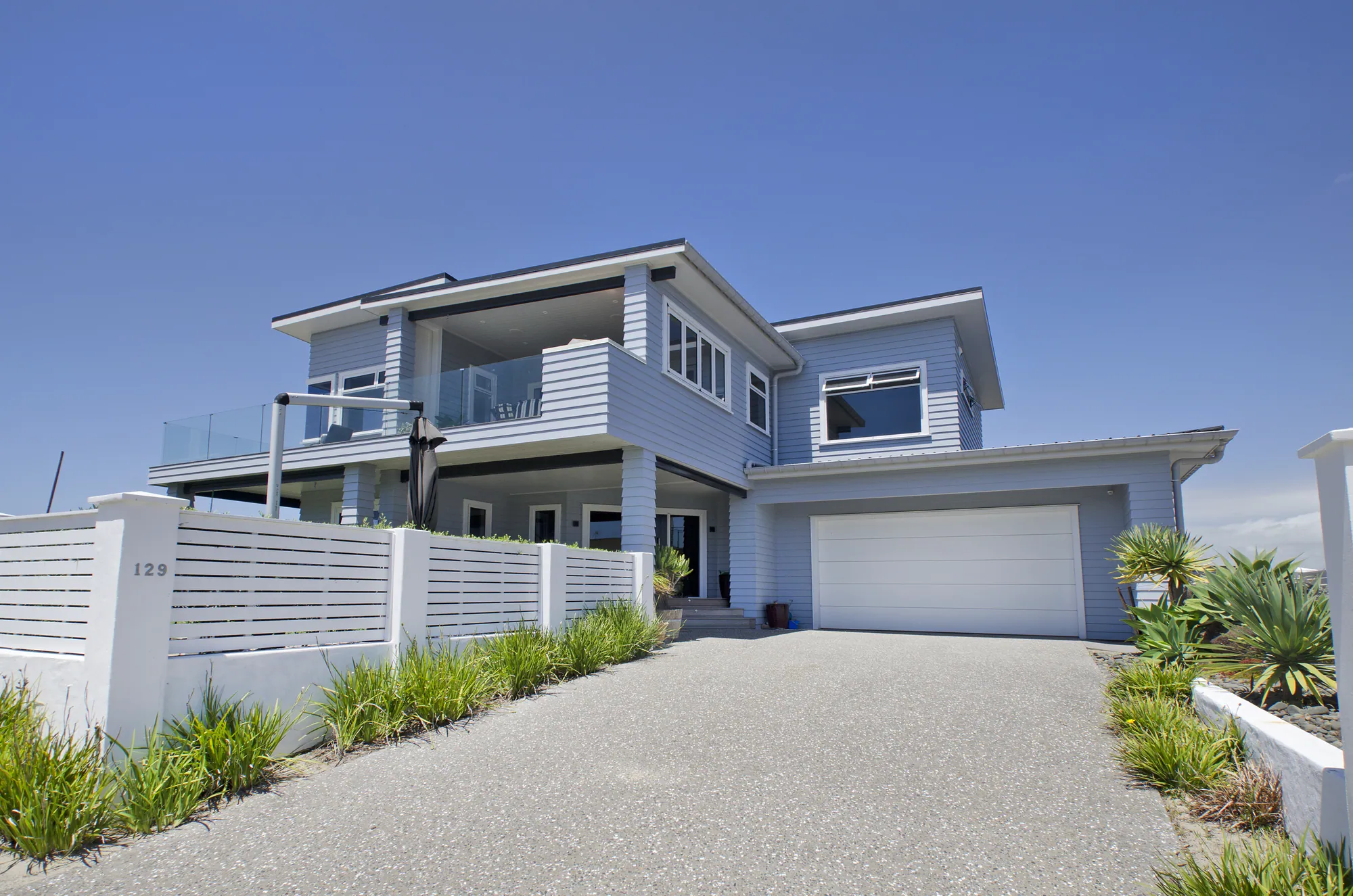 The same Bream Bay Drive house after recladding, in pale weatherboard with new glazed balustrades